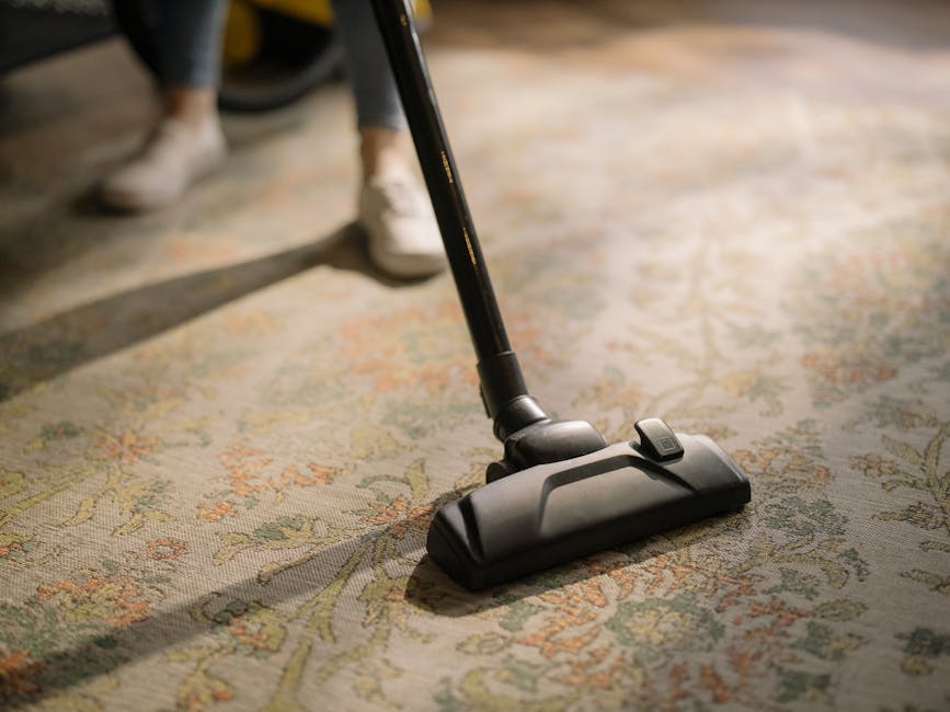 A professional cleaning technician from Carpet Cleaning Brixton is performing deep carpet cleaning in a bright, modern living room. The technician is dressed in a full white protective suit, including